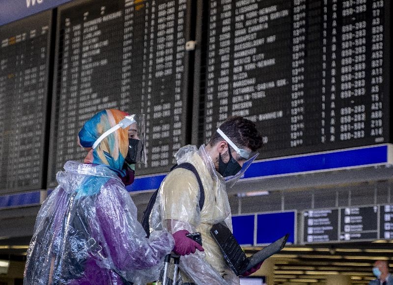 Passengers with protection gear walk past the flight board at the airport in Frankfurt, Germany. (Photo by Michael Probst/AP Photo)